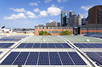 Solar panels on the roof of a building with skyscrapers in the background.