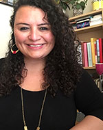 Marcia Vera Espinoza in front of a bookcase, wearing a black top and hoop earrings