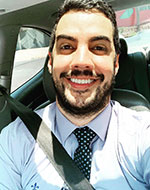 Renan Antônio da Silva, in a car wearing a seatbelt. He's wearing a blue shirt with a navy blue tie with a light blue diamond pattern.