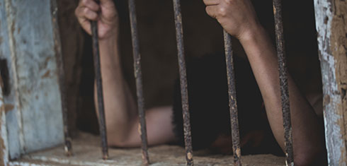 Boy in a cell clinging onto rusty prison bars