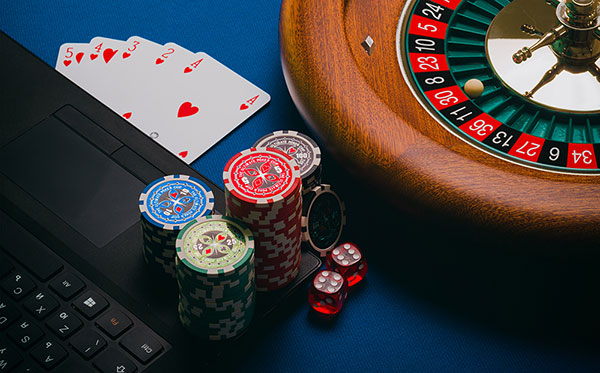 A laptop sat next to a Wheel of Fortune, some playing cards and gambling chips