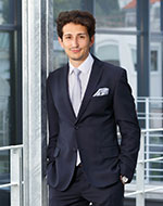 Full body image of Marek Anderle in a suit against an office window