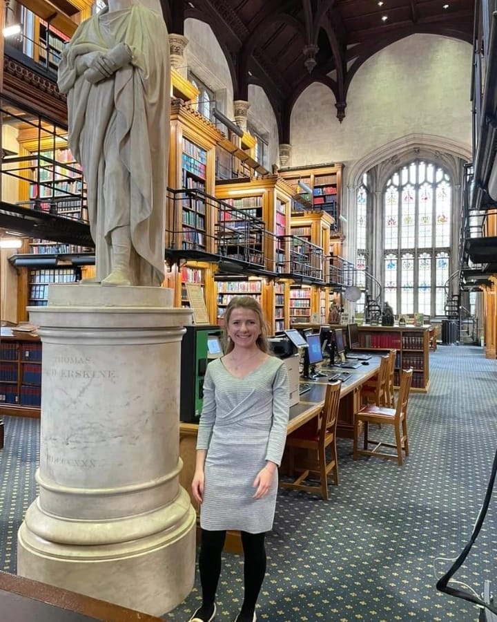 Lisa in a grey dress standing next to a statue in the library