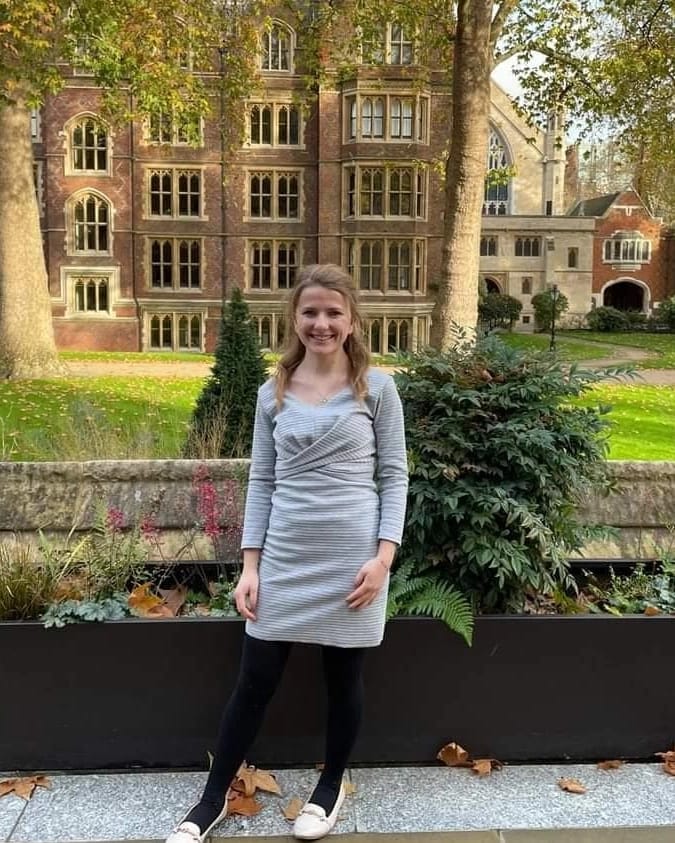 Lisa in a grey dress standing in a university courtyard in summer