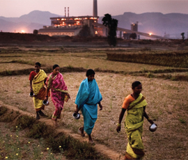 Indian women walking through a field in front of a factory