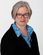 Julia Hornle wearing glasses, a black jumper and pearls