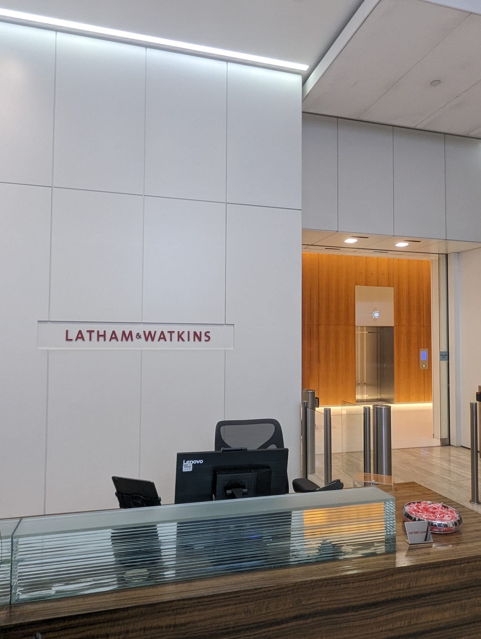 The lobby area at Latham and Watkins law firm with an empty desk, chair and a white wall with red Latham and Watkins logo