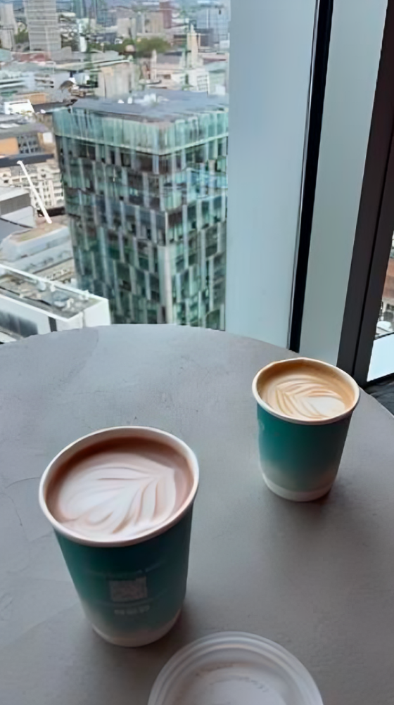 Two coffee cups on a table with a view from the window showing another skyscraper