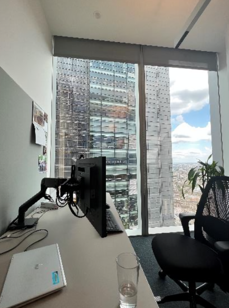 Office at a law firm with a desk, chair and computer. The view from the large window shows another skyscraper right next to this office building