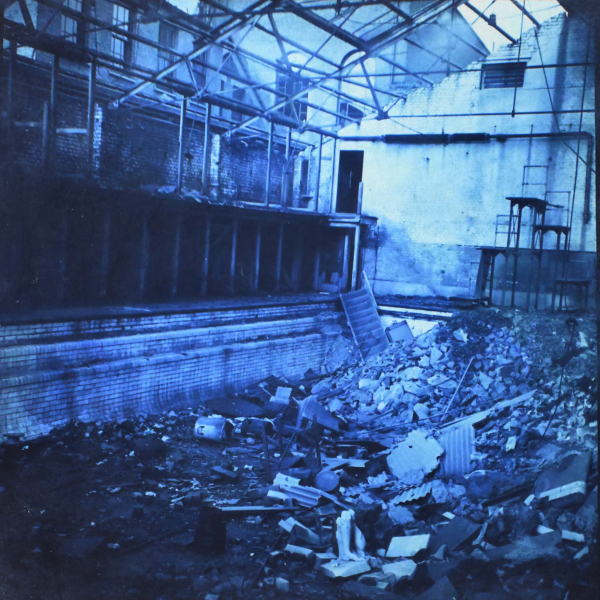 Photograph showing Swimming pool after bombing, a large pile of rubble and other items in the pool and the roof open.