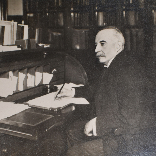 Professor Hatton sitting writing at his desk in a room with book shelves