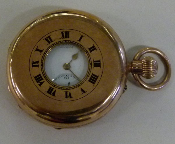 Colour photograph of a gold pocket watch.  The watch is roman numerals in black inscribed on the gold case surround a small dial face