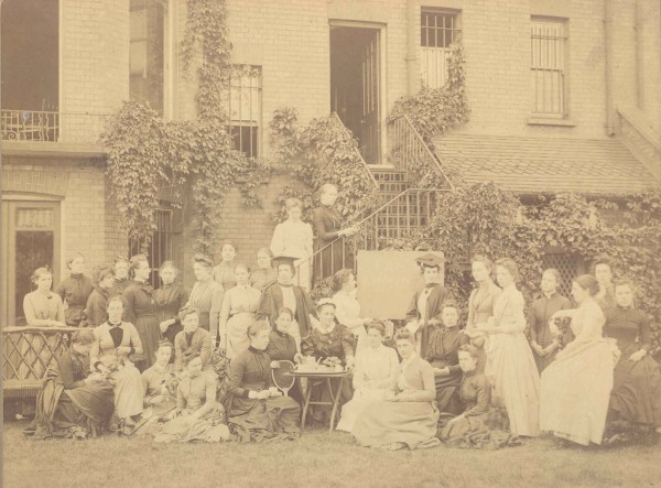 Sepia photograph from 1889 of a group of women sitting outside.  Some are seated on the grass, whilst others sit on chairs or benches