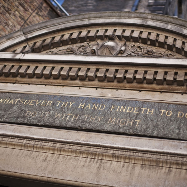 Close up of a quotation in gilt lettering on a grey stone plaque above the door of the Museum and Library Block at St Bartholomew's Hospital in London