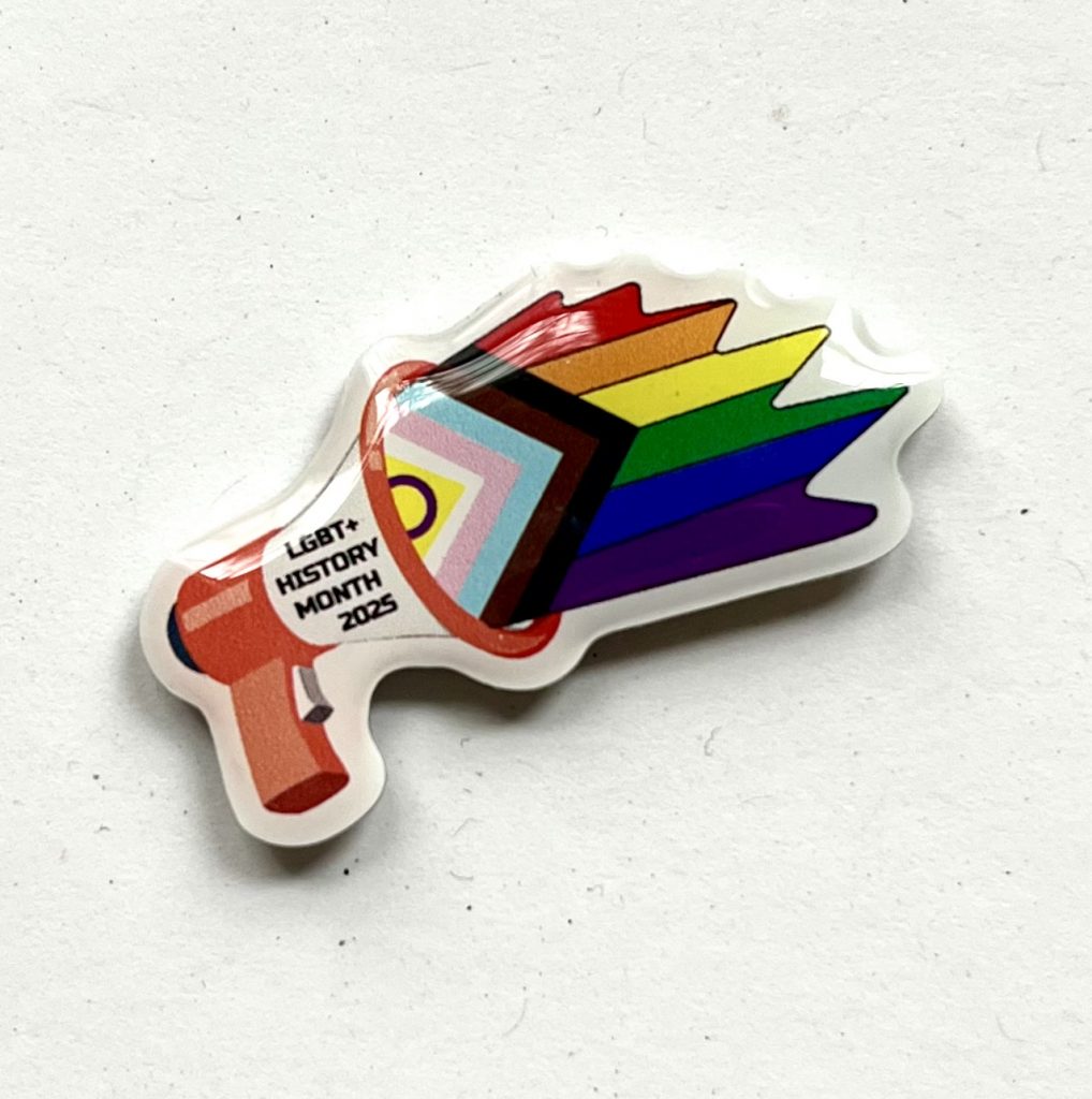 An enamel badge in the shape of a megaphone that is blasting the Intersex Inclusive Progress Pride flag