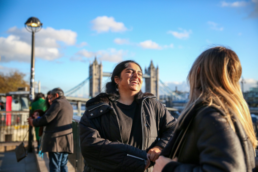 An image of two students laughing in front of tower bridge