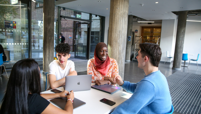 A group of students sitting on a table chatting with laptops on the desk