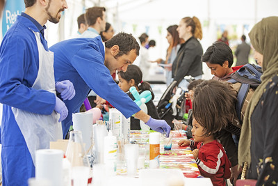 A Queen Mary staff member uses dye to colour water as children watch at the Festival of Communities