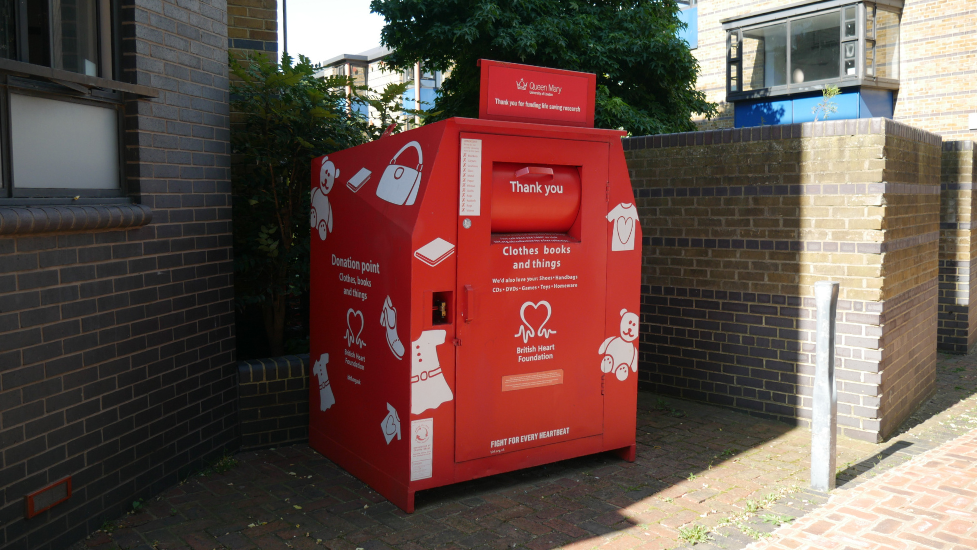 A red British heart foundation bin in a paved area