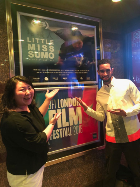 Photo of alumnus, Matt Kay, with Sumo star, Hiyori Kon, standing by a poster for their film