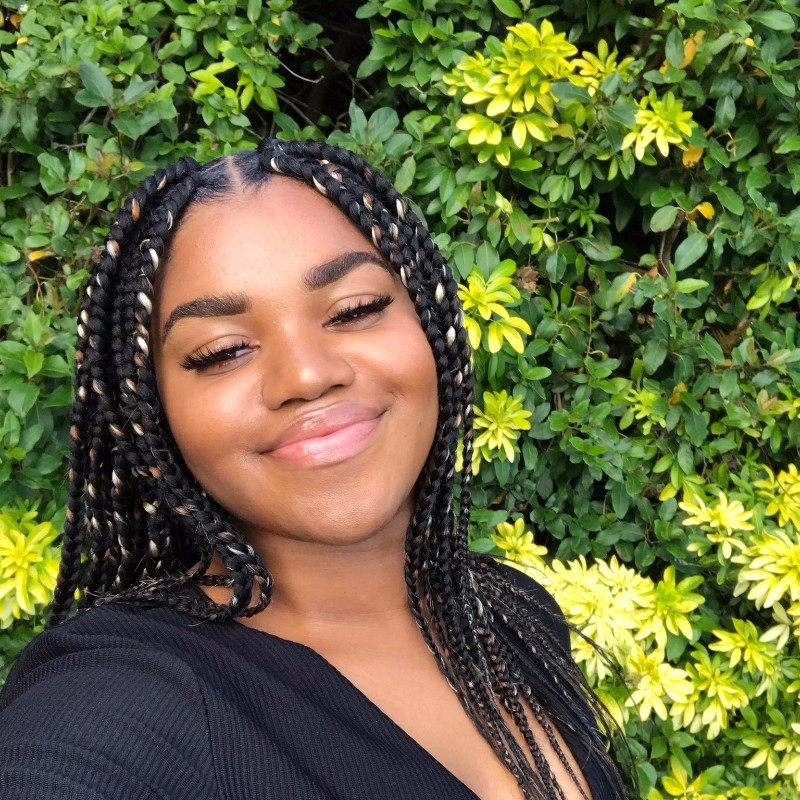 Selfie-style photo of Naila Barrett. She is standing in front of a hedge and is smiling.