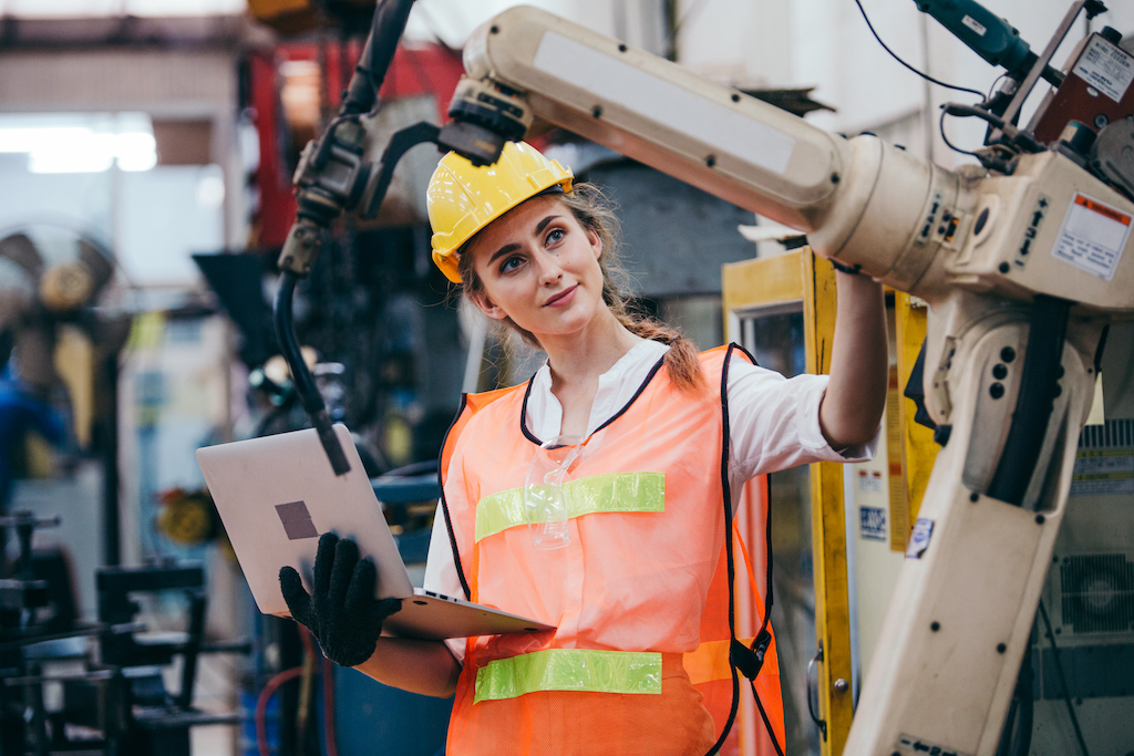 Woman holding laptop and inspecting machinery