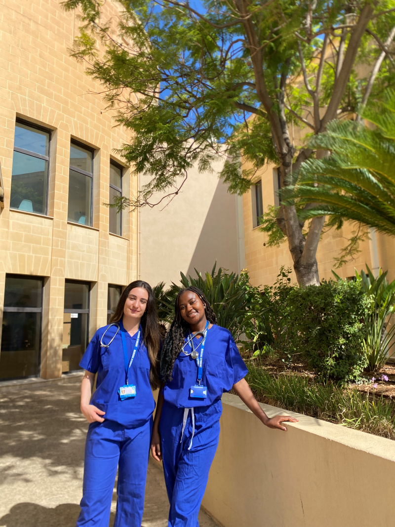 Lydie and Hazal in blue scrubs outside building in the sunshine