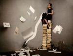 Stock image of a woman sitting on a pile of books whilst typing
