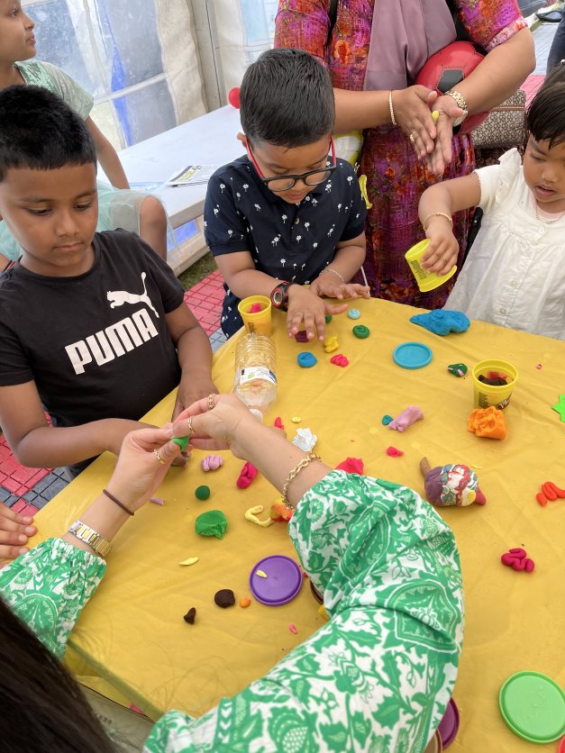 Three young children making brains out of play doh with the help of a researcher. The brains are brightly coloured against a yellow tablecloth.
