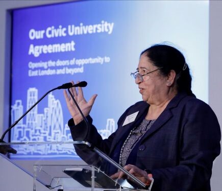 A woman talks at a podium in front of a presentation which says 'Our Civic University Agreement'.