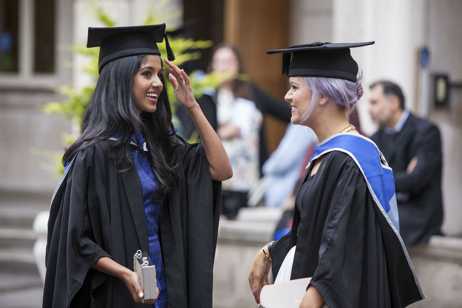 Students talking to each other wearing graduation gowns