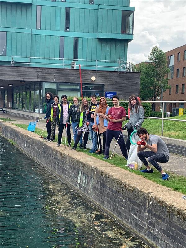 Students standing by the canal on campus after cleaning up the litter with nets and litter pickers.