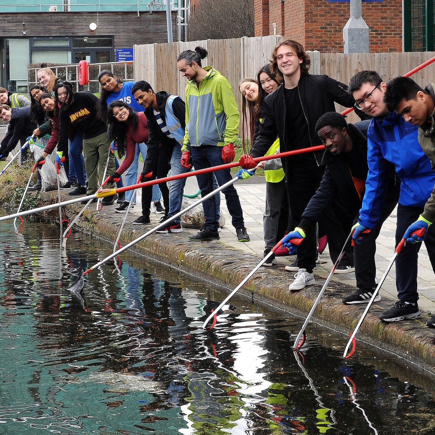 A large group of students with litter pickers and nets posing next to Regent's Canal after litter picking.