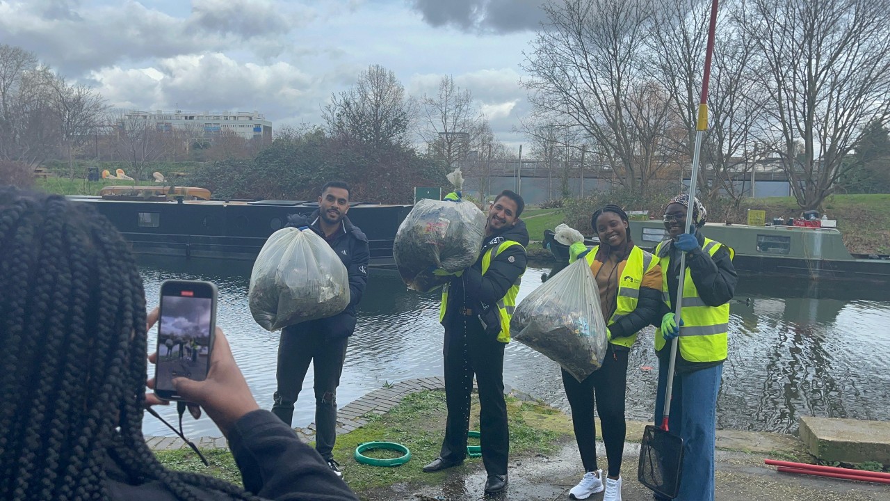 A group of four students with full bags of rubbish posing next to Regent's Canal on the Mile End Campus after cleaning the canal as part of Climate Action Week.