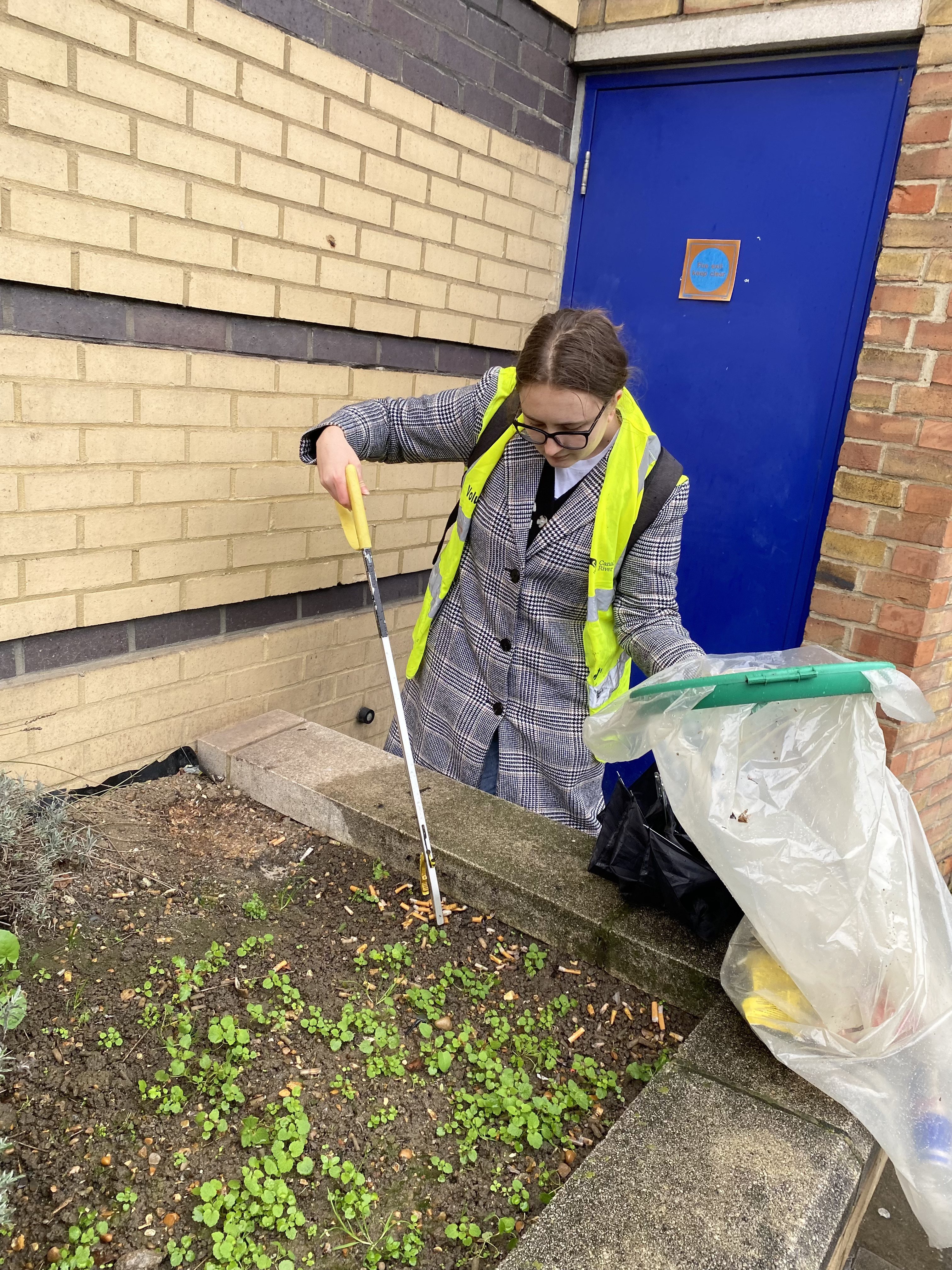 Student litter-picking outside the Mile End campus as part of Climate Action Week, picking up a large pile of cigarettes from a planter box.