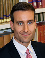 Headshot of Davor Jancic wearing a suit in front of a bookshelf