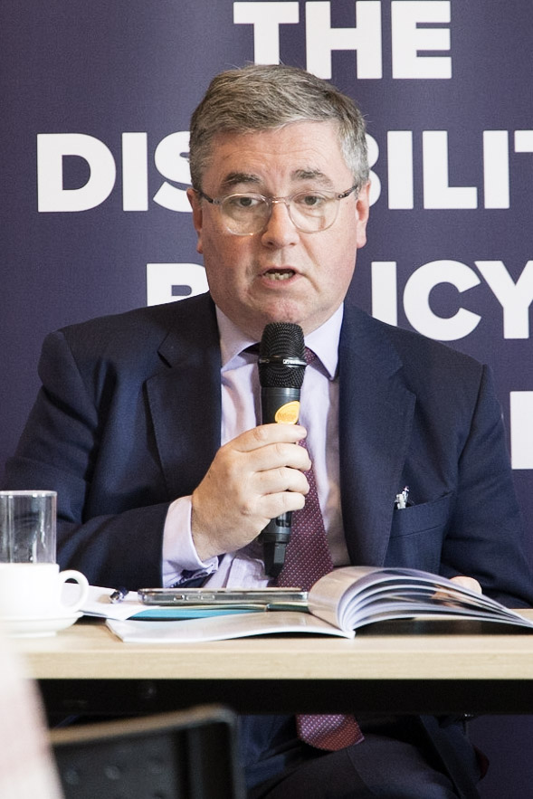 Sir Robert Buckland speaking at the Mile End Institute on 22 May. He is wearing a dark suit and holding a microphone and is looking directly into the camera.