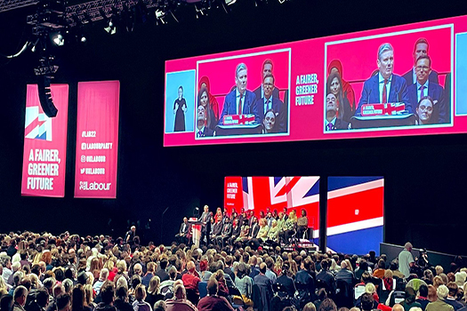 Photo of Keir Starmer's speech at the Labour Party conference in 2022. It is taken from the back of the auditorium and shows the audience listening to Keir Starmer