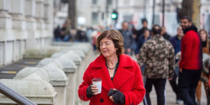 Photo of Sue Gray outside the Cabinet Office on Whitehall. Gray is wearing a bright red overcoat and carrying a takeaway coffee. Credit to Alamy.