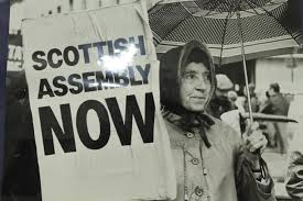 Photo of elderly Scottish woman holding a 'Scottish Assembly Now' sign.