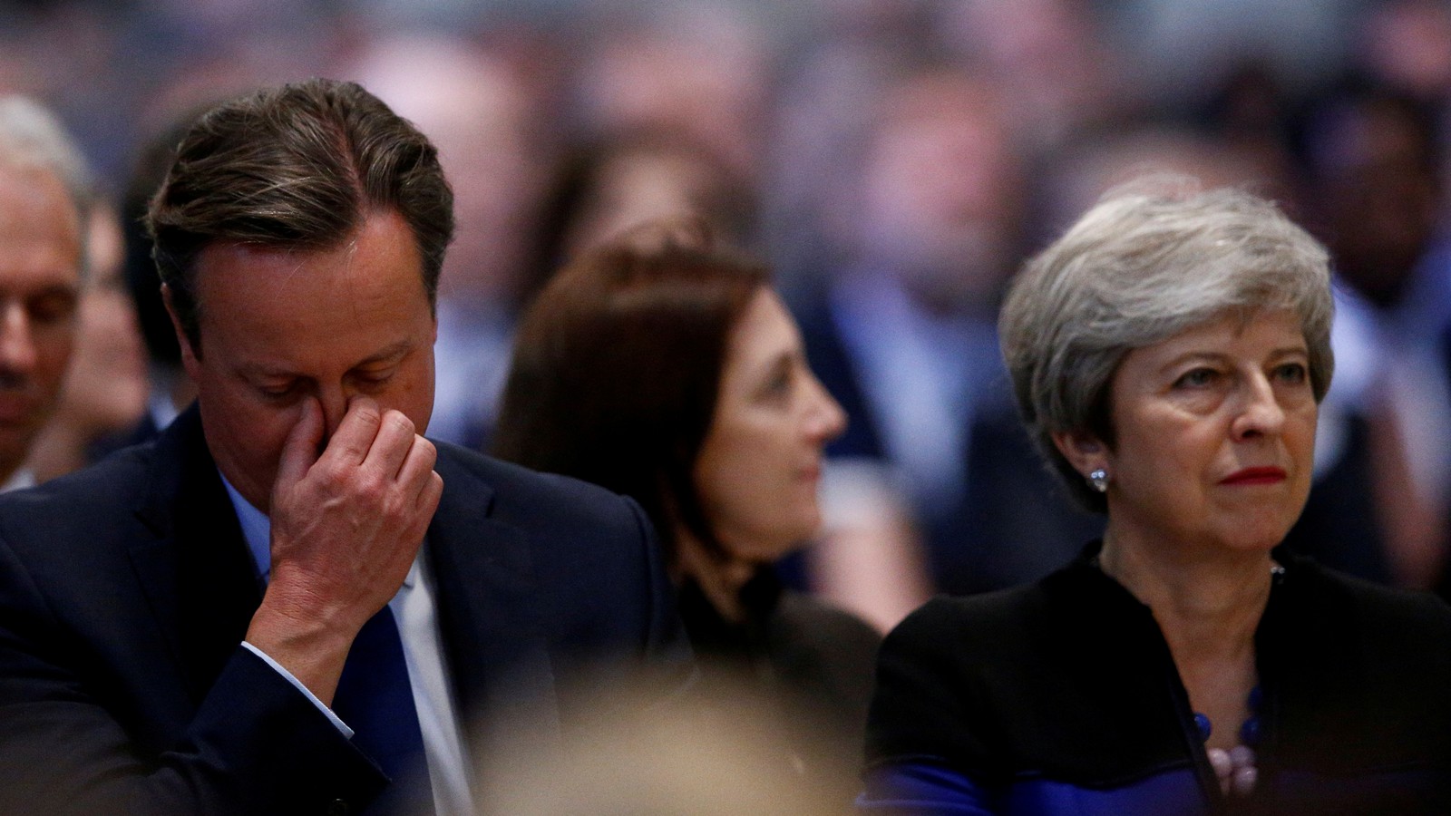 Photo of David Cameron, head in hands, sitting next to Theresa May in the audience at a Conservative Party conference