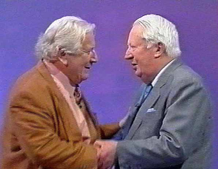 Peter Ustinov embracing the former Conservative Prime Minister, Sir Edward Heath. The two men are looking into each other's face and are standing in front of a purple screen. It was taken during Ustinov's appearance on This Is Your Life in 1994.