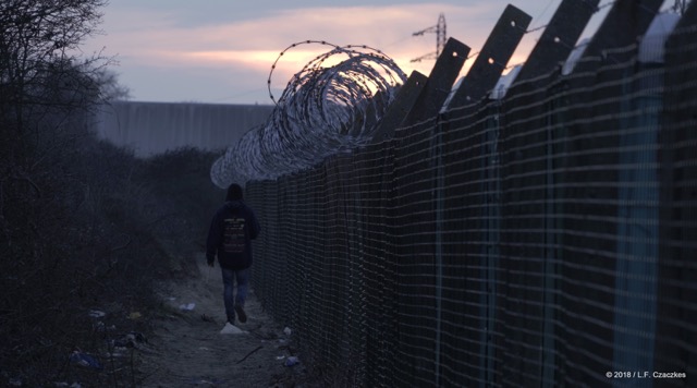 figure walking away next barbed wire fence in evening