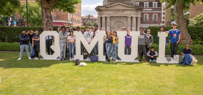 A group of students standing behind large letter blocks QMUL