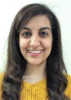 A close-up head and shoulders shot of Aiya Al-Jabiri. She has long medium brown hair that curls slightly, dark brown eyes and olive skin. She is wearing a mustard yellow top. She is smiling for the camera.