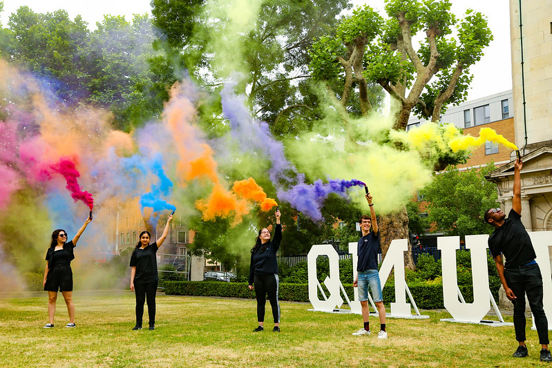 Students standing in front of QMUL sign holding coloured flares