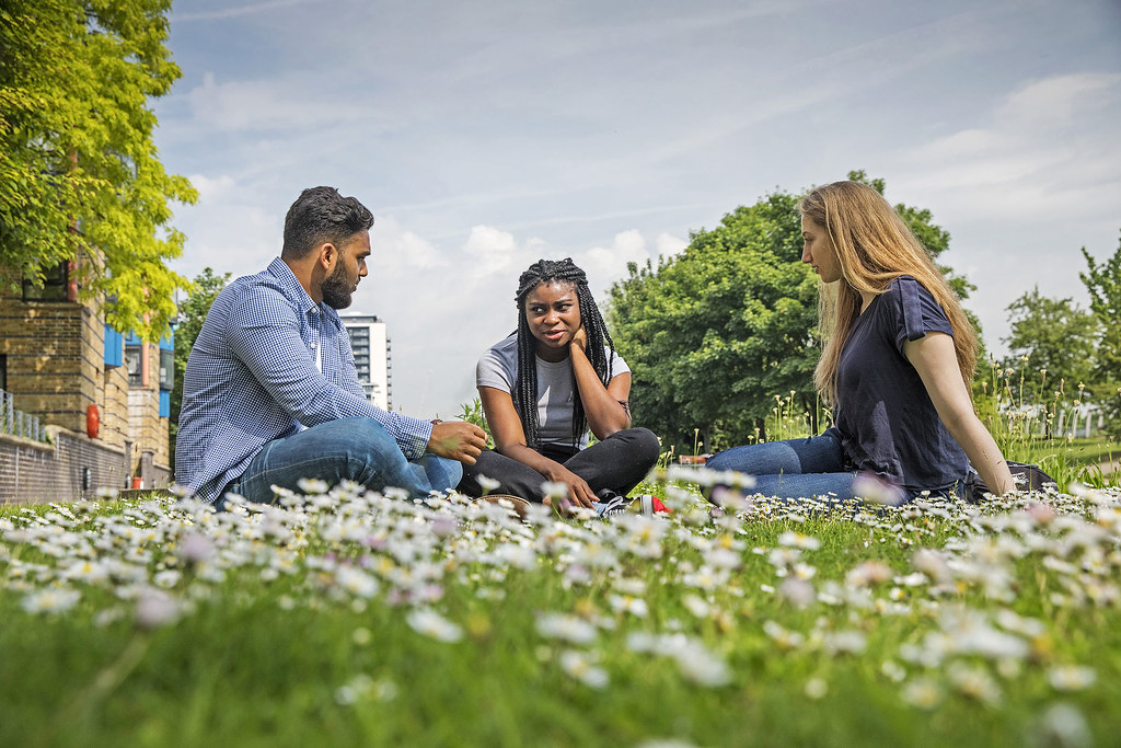 Three students sitting on the grass chatting in the sunshine