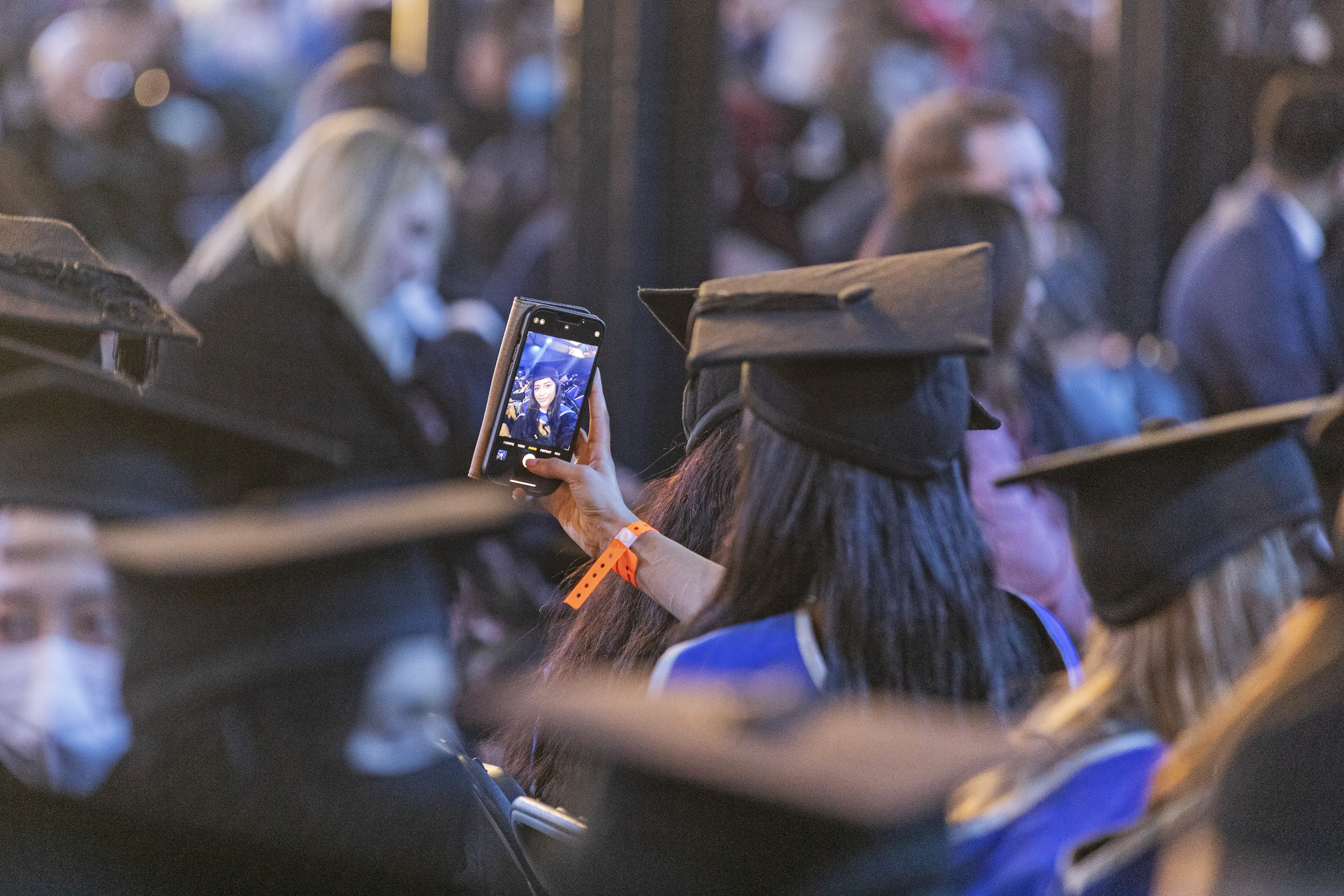 A student at graduation pictured from behind, taking a selfie