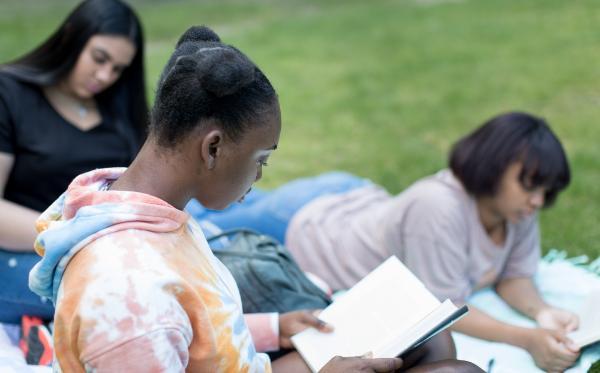 Three young women sitting on a lawn reading books