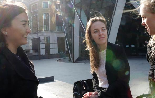 Three women in conversation on benches outside the Gherkin in the City of London